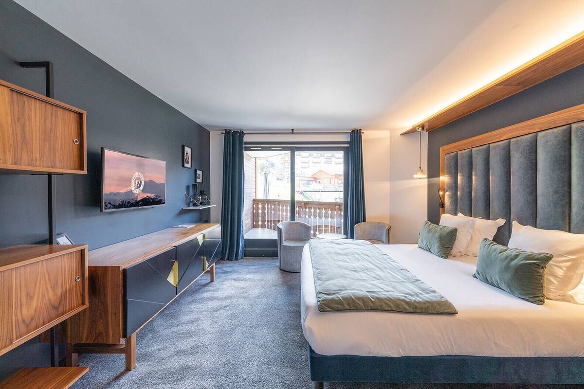 A modern hotel room with a bed, desk, and a balcony with a view.