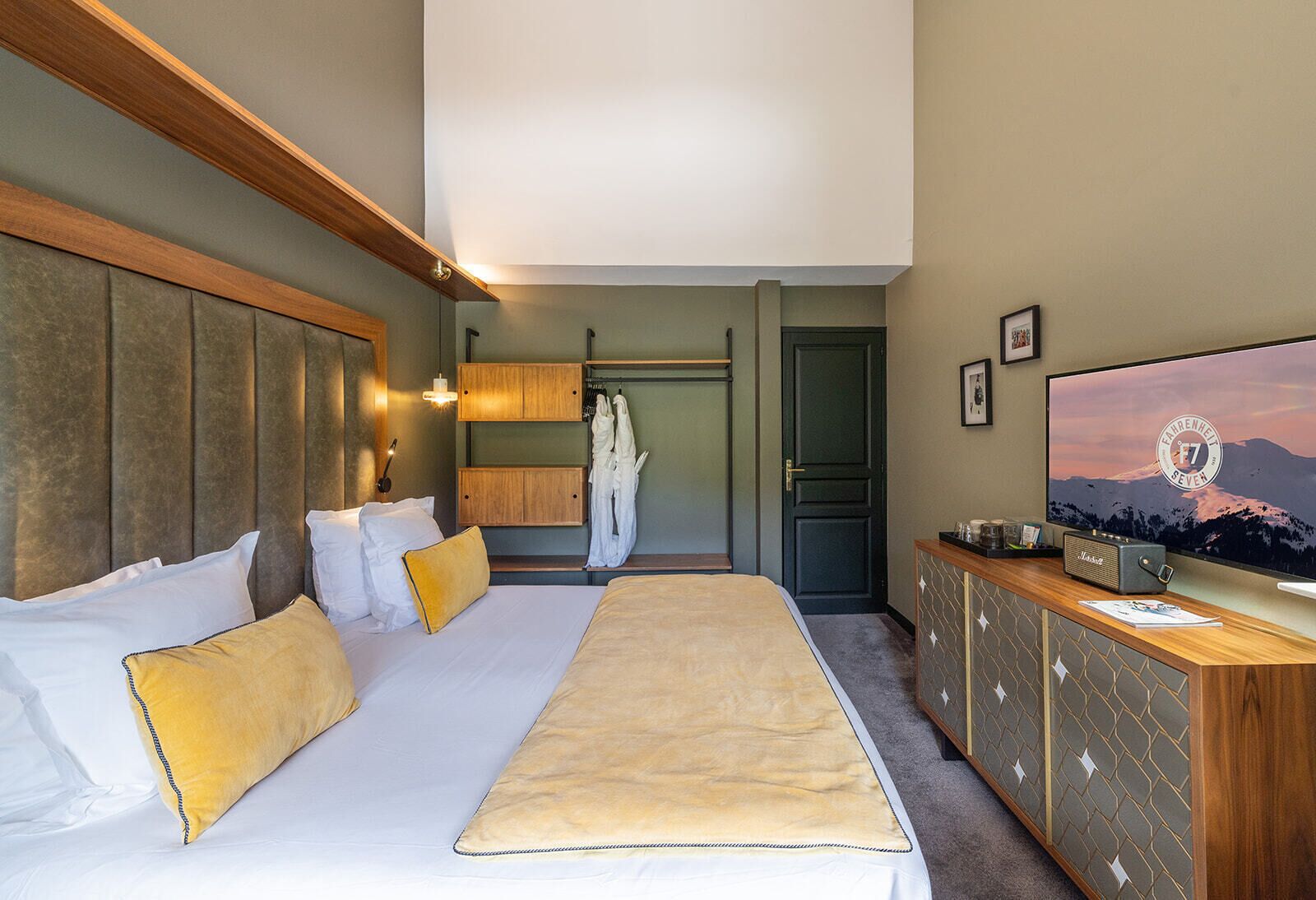 A hotel room with a bed, bedside tables, a wardrobe, a television, and a view of a mountain.