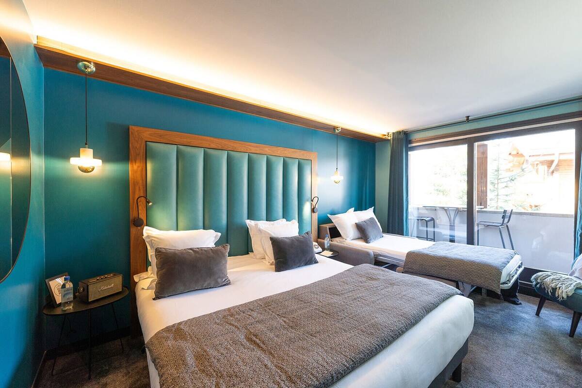A hotel room with two beds, a wooden headboard, a small table with a radio, and a balcony with chairs.
