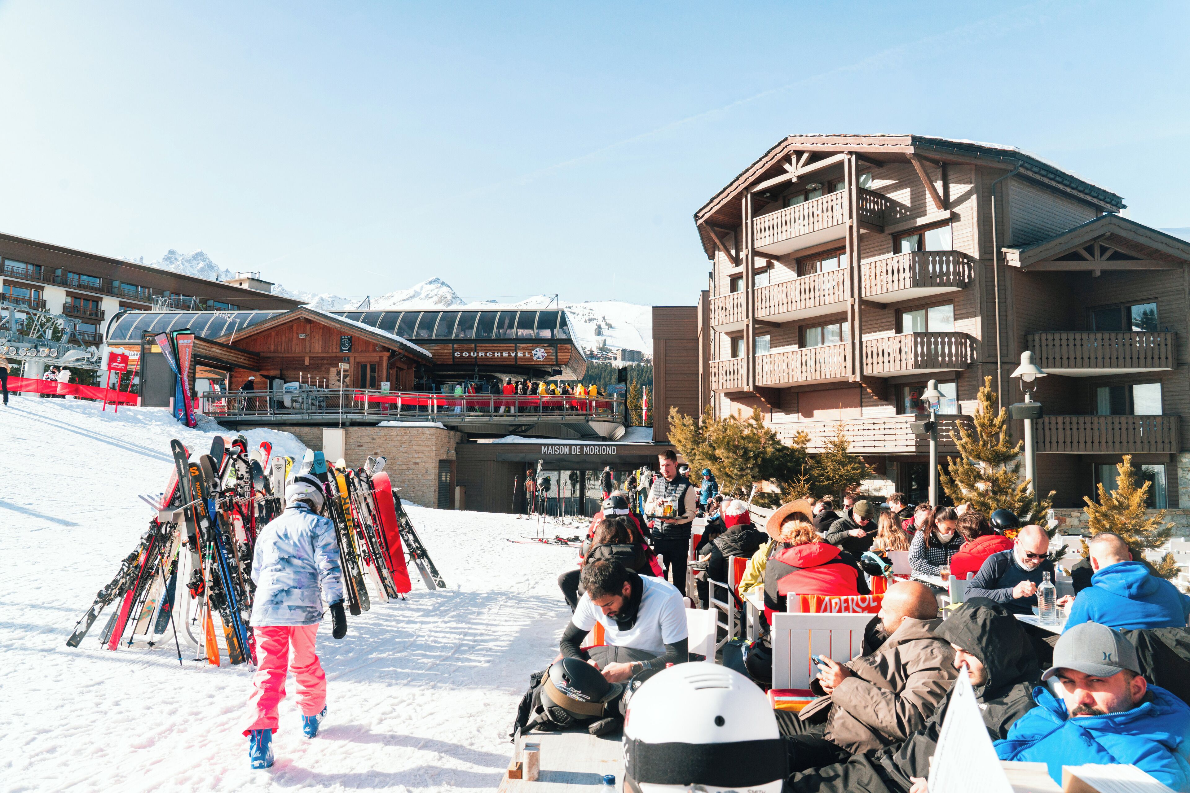 A ski resort with a wooden building, a ski lift, and a crowd of people.