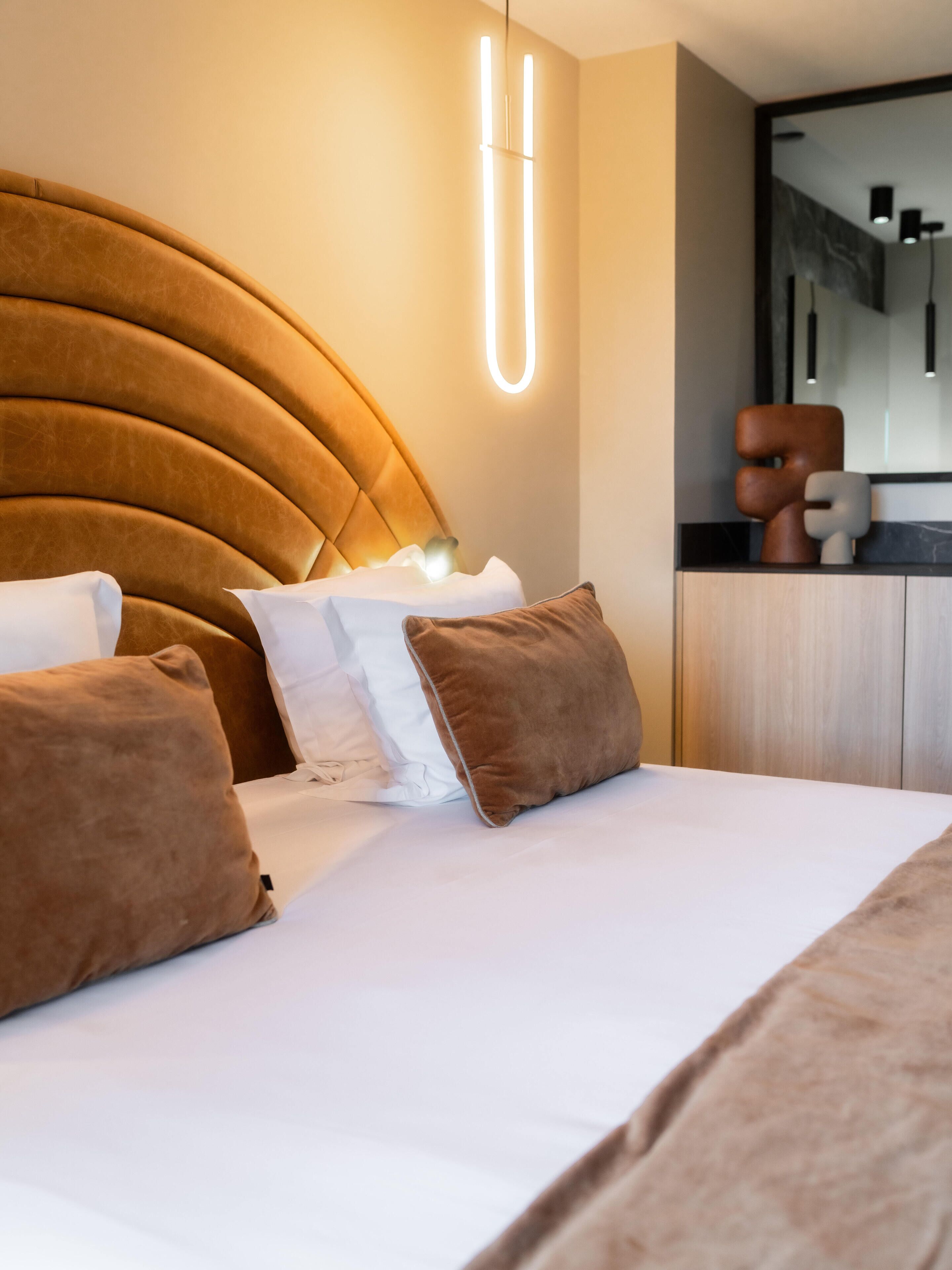 A modern bedroom with a curved headboard, a bedside table, and a mirror.