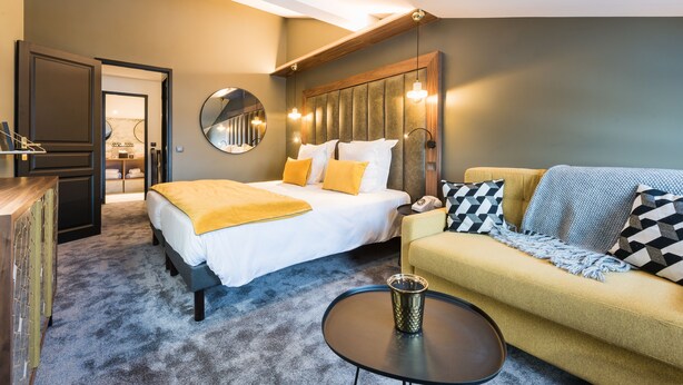 A hotel room with a bed, a sofa, a coffee table, a mirror, and a wooden headboard. - Fahrenheit seven Courchevel (Courchevel)