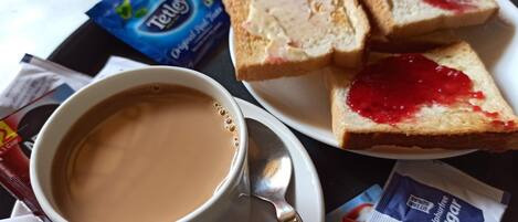 Eine Tasse Kaffee mit Löffel, ein Teller mit zwei Scheiben Brot mit Marmelade sowie Teebags und Zucker auf einem Tisch.