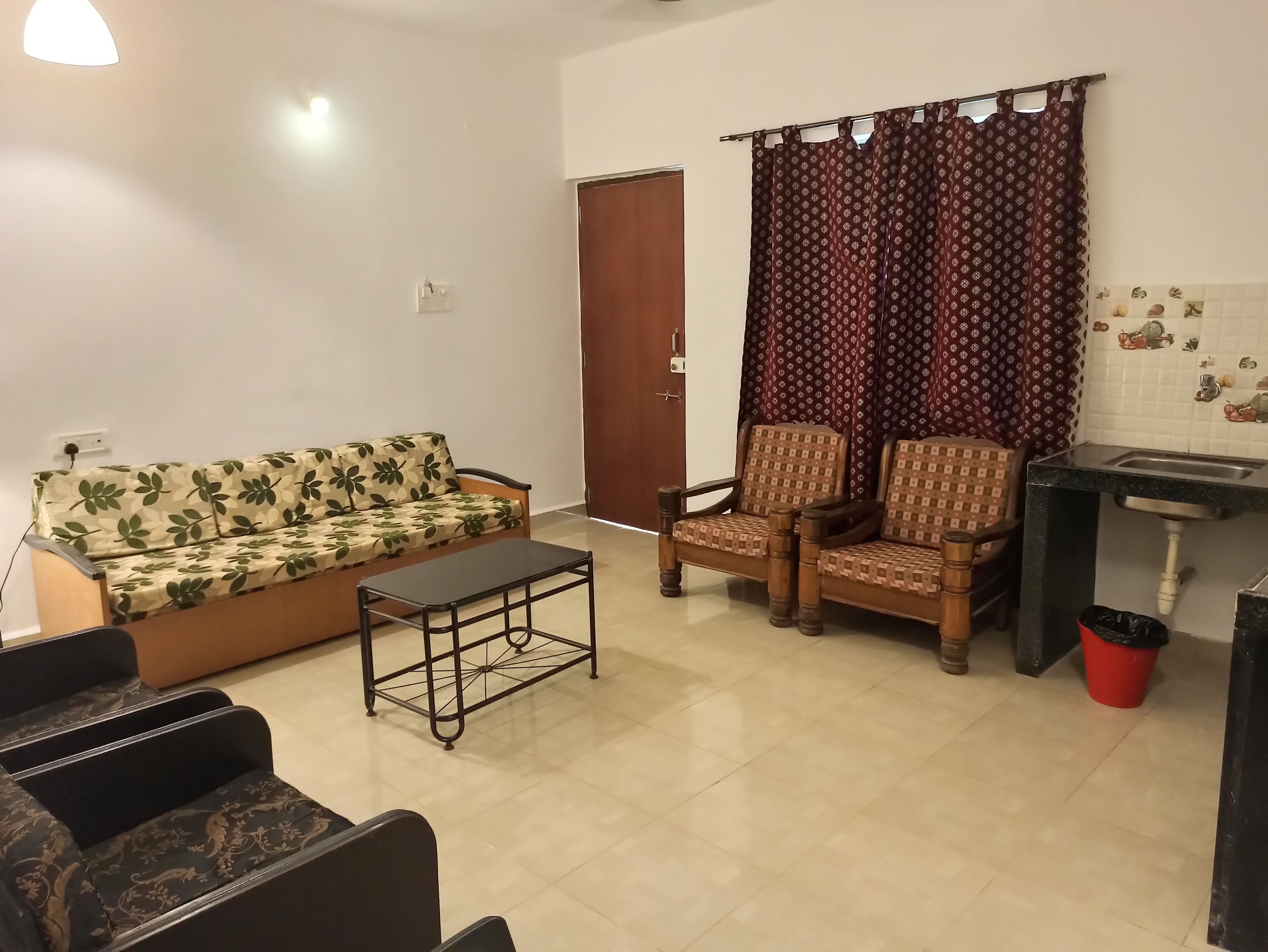 A living room with a sofa, two armchairs, a coffee table, a door, and a kitchen area with a sink.