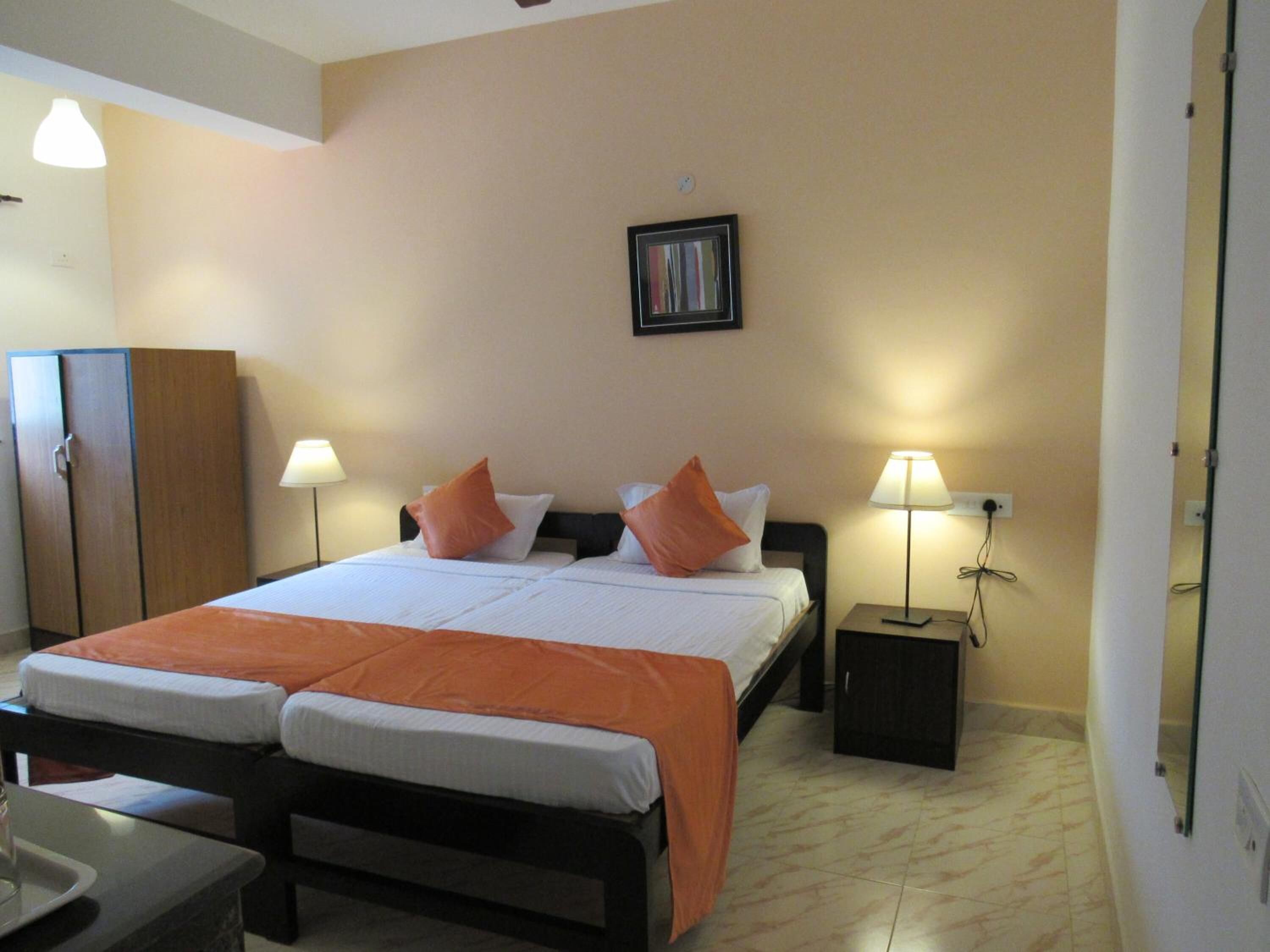 A hotel room with two beds, a wardrobe, bedside lamps, and a framed picture on the wall.