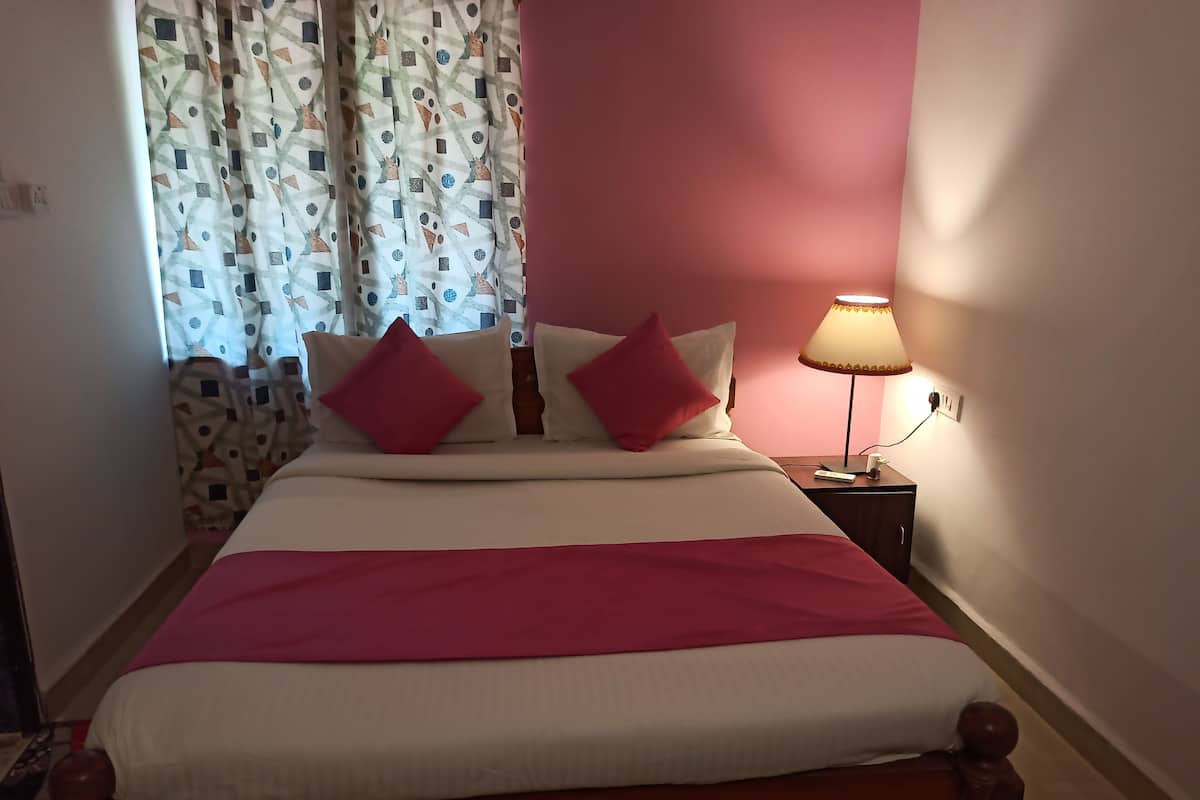 Een bed met een rood-wit sprei, twee rode kussens en een nachtkastje met een lamp.