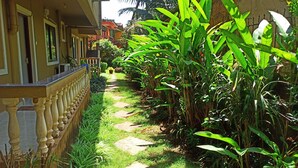 Un sendero estrecho bordeado de abundante vegetación y un edificio con balcones.