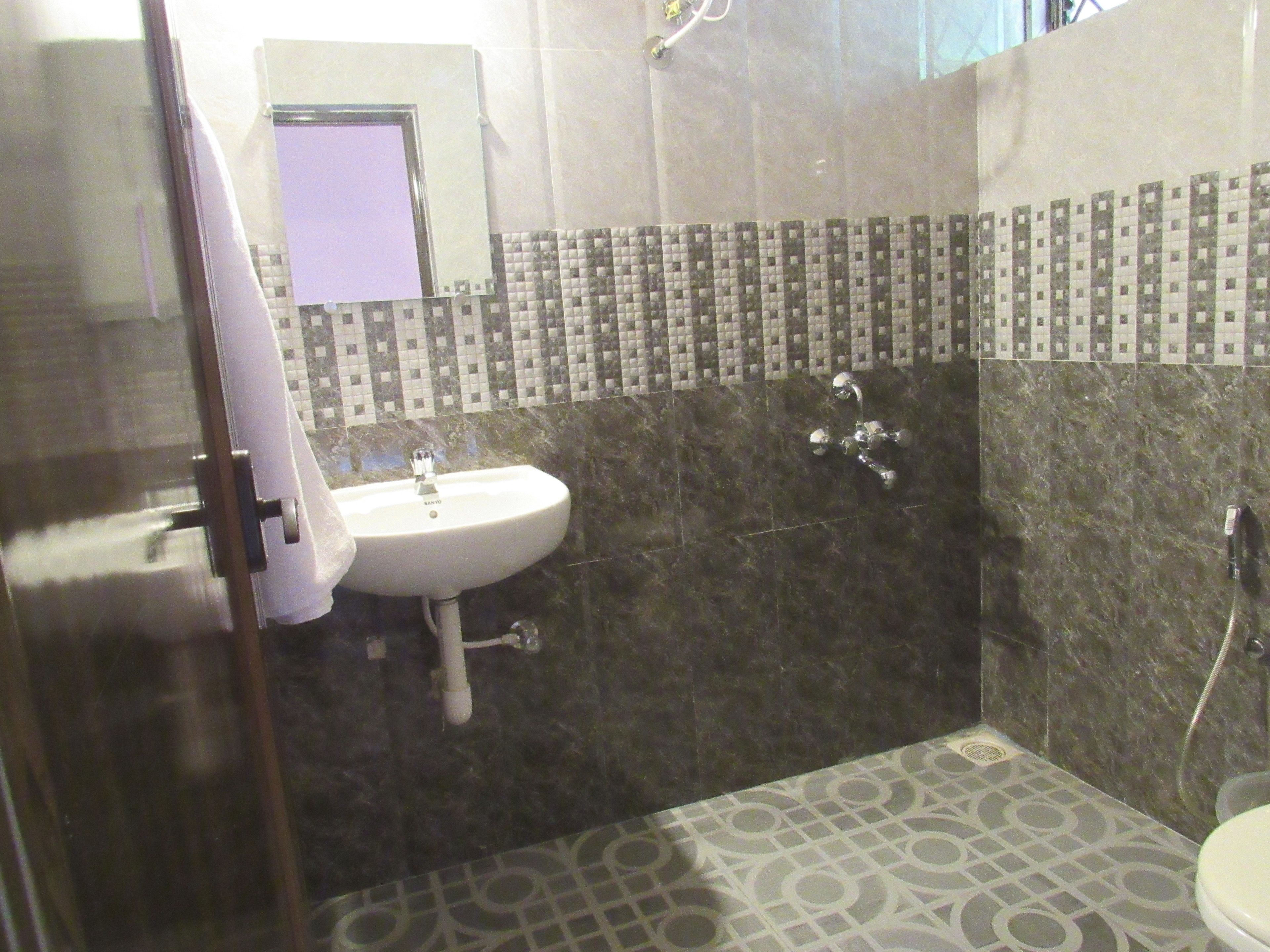 Un baño con lavamanos, espejo, ducha y baldosas de suelo estampadas.