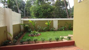 A small, enclosed garden area with a paved walkway, surrounded by a low wall and various plants.