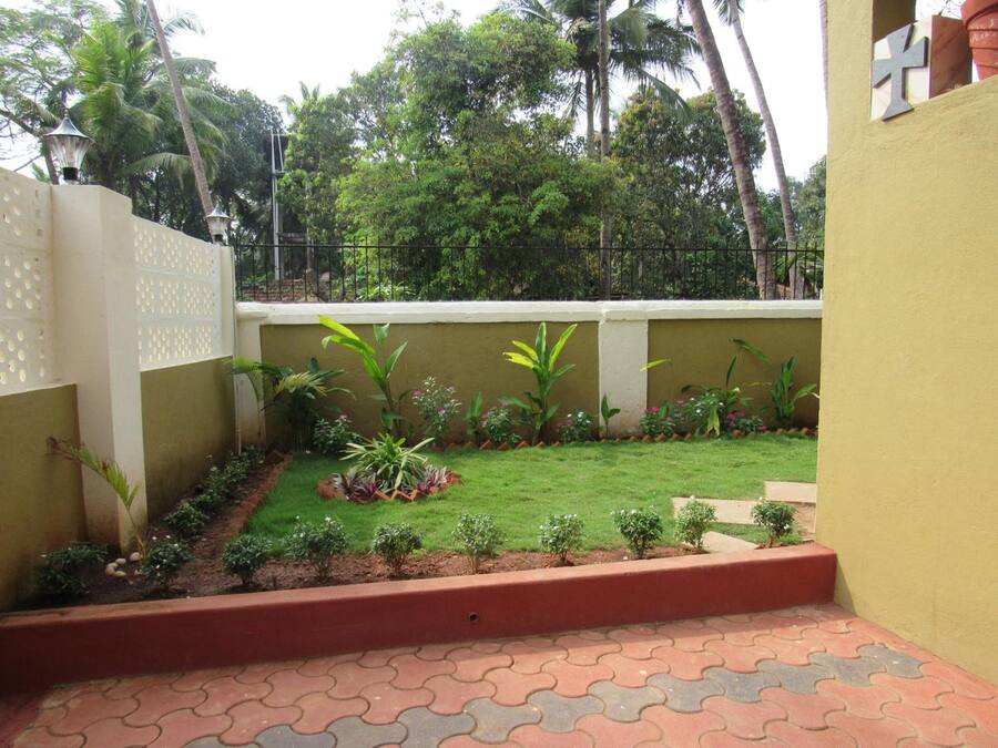 A small, enclosed garden area with a paved walkway, surrounded by a low wall and various plants.