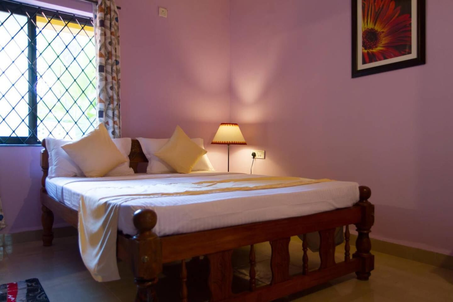 Une chambre à coucher avec un lit en bois, du linge de lit blanc, une lampe de chevet et une fenêtre avec un rideau.