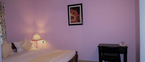A bedroom with a bed, a nightstand, a desk, a ceiling fan, and a wall-mounted picture.
