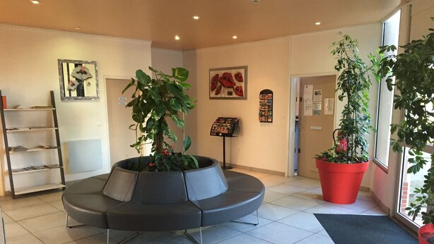 A reception area with a modern seating arrangement, a potted plant, a reception desk, and a wall-mounted information board.