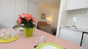 A small, neatly arranged room with a dining table set for two, a bed, and a kitchenette. - ABITEL - Les Studines d'Ornon (Villenave-d'Ornon)