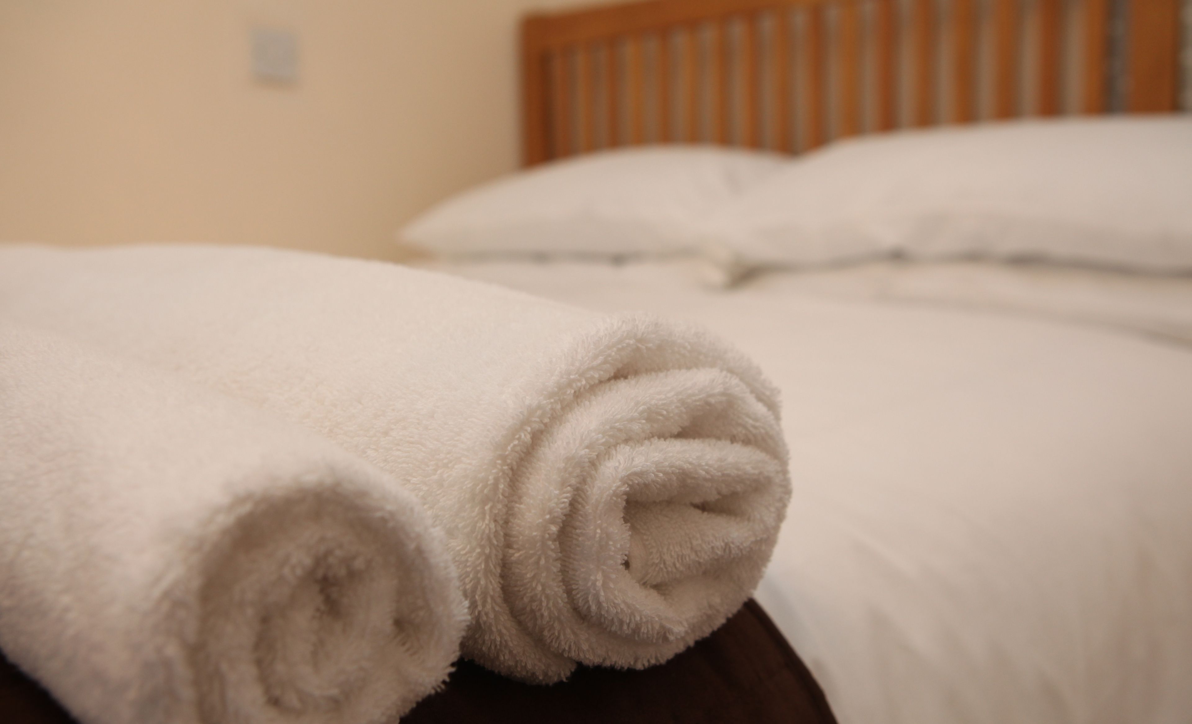 A neatly made bed with white linens and a rolled white towel on the side.