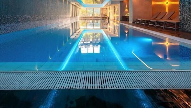 A modern indoor swimming pool with a central viewing area, surrounded by seating and a high ceiling. - Grand Hotel Belvedere Brasov (Brasov)