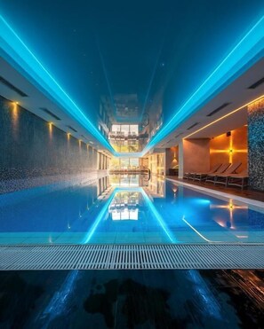 Una piscina interior moderna con una zona central de observación, rodeada de asientos y un techo alto.