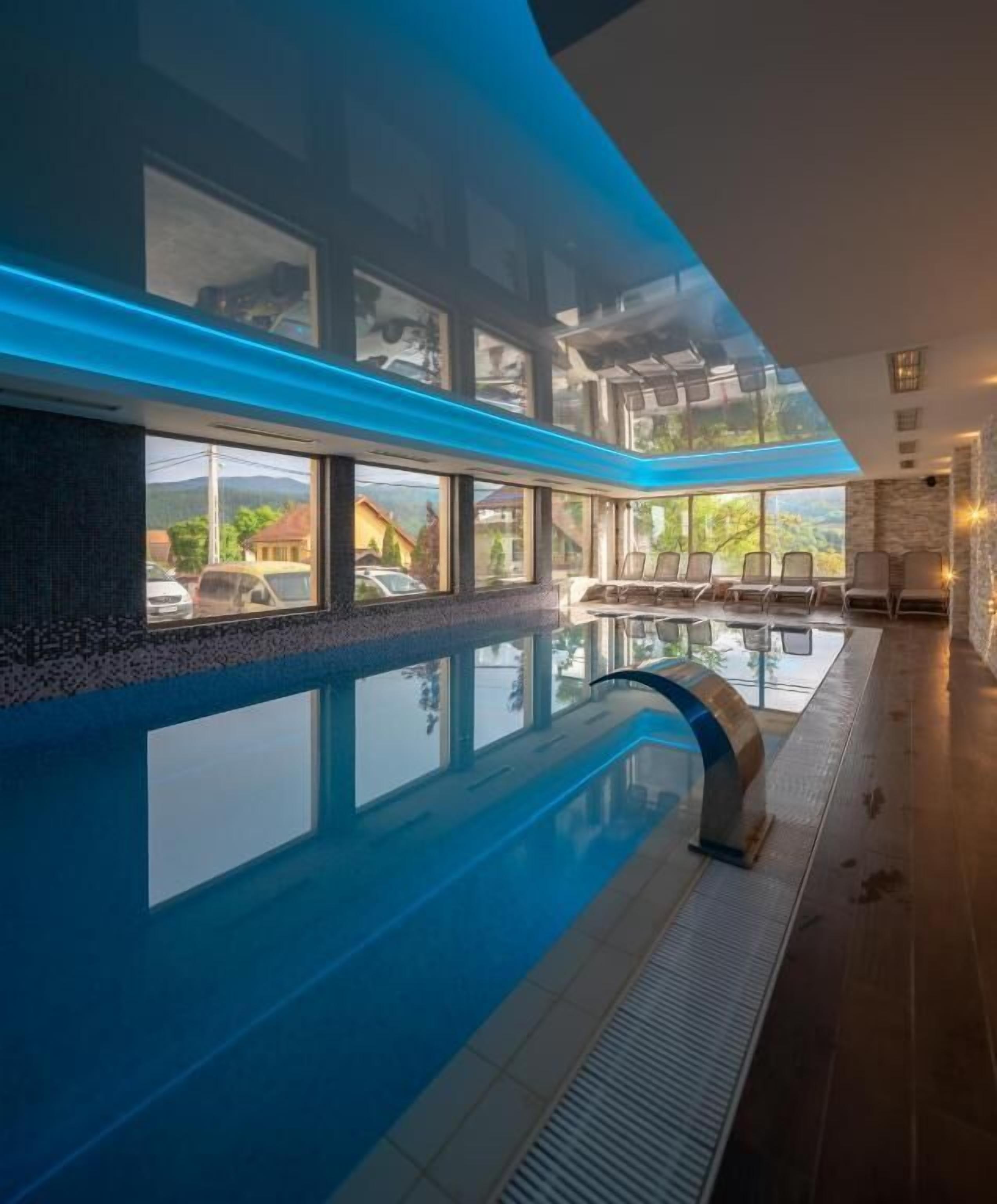 Una piscina interior con paredes de vidrio transparente, un área de descanso con sillones y vistas al exterior.