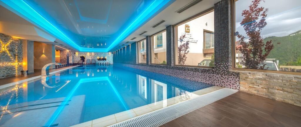 En swimmingpool med blått ljus, en stenmur och utsikt över ett berg.