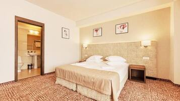 A hotel room with a bed, a bedside table, a mirror, and framed pictures on the wall.