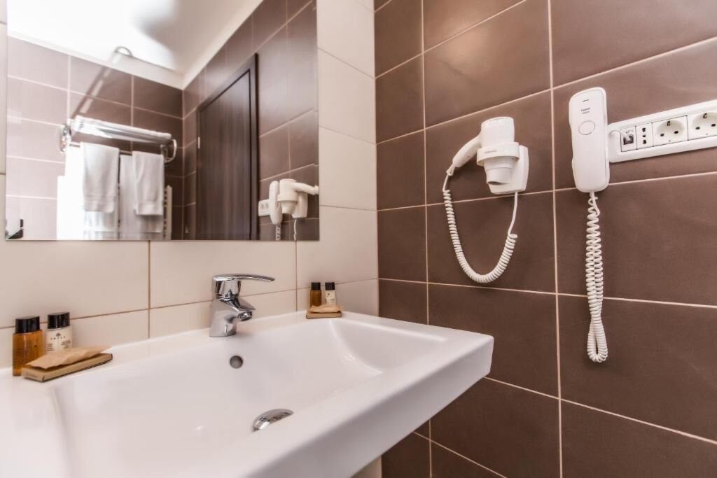 Un baño con lavamanos blanco, un espejo, toallero y teléfono instalado en la pared.