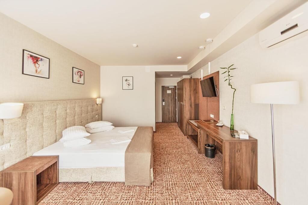 Habitación de hotel con una cama grande, un escritorio de madera, un televisor y aire acondicionado instalado en la pared.