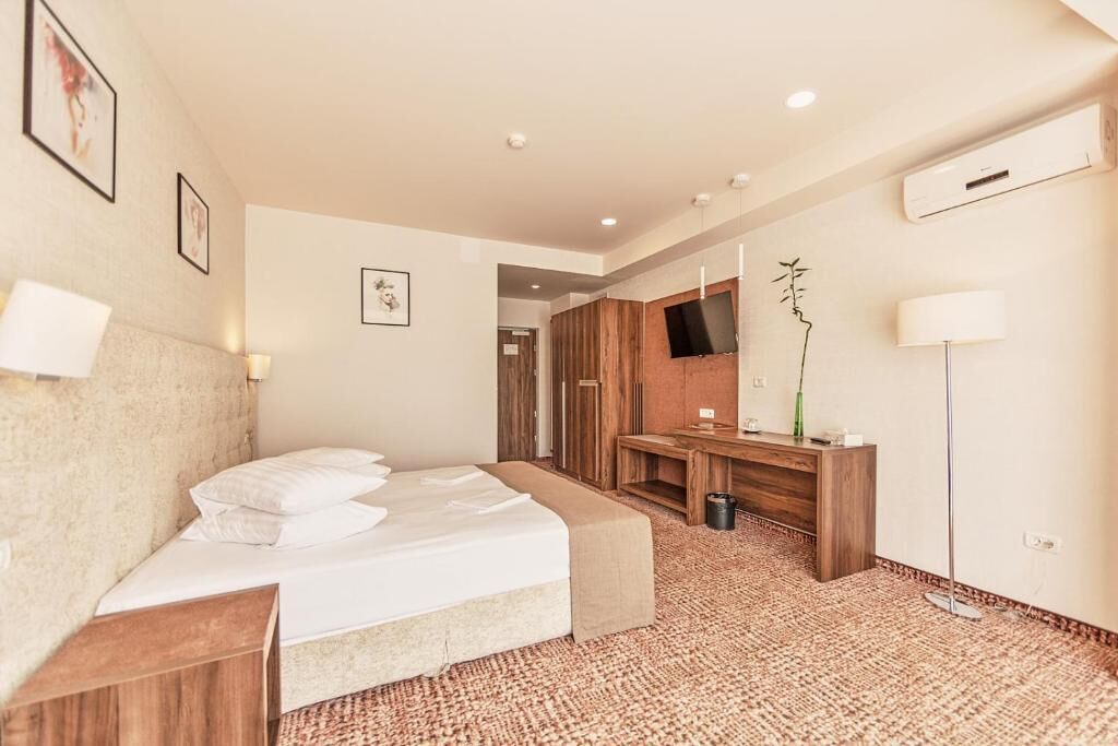 Ein Hotelzimmer mit Bett, Nachttisch, Schreibtisch mit Stuhl, einem an der Wand montierten Fernseher und einem großen Spiegel.
