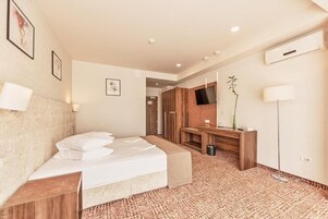 Habitación de hotel con cama, mesita de noche, escritorio con silla, televisor montado en la pared y un espejo grande.