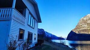 A white house with a balcony, a river, and mountains in the background. - Visit Undredal (Aurland)