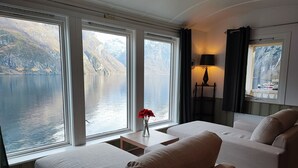 A modern room with large windows offering a view of a lake and mountains. There are two sofas and a small table with a vase of flowers. - Visit Undredal (Aurland)