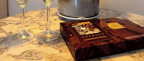Dos copas de vino blanco, una botella de champán y una caja de bombones sobre una mesa de mármol.
