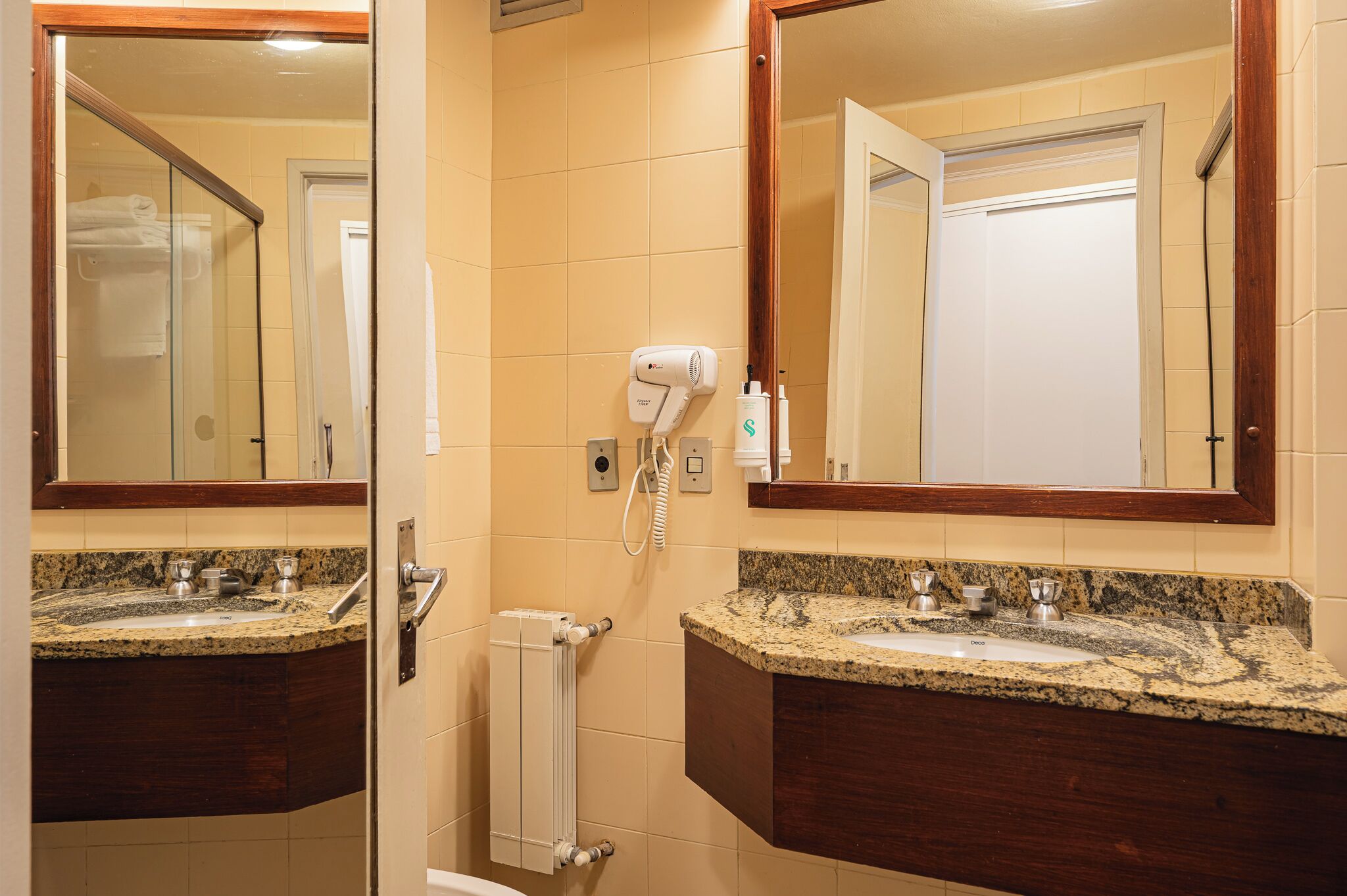 Un baño con dos lavamanos, un secador de pelo y un espejo.