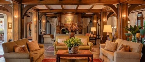 A spacious living room with a high ceiling and wooden beams, featuring a central coffee table, two sofas, and a decorative vase.