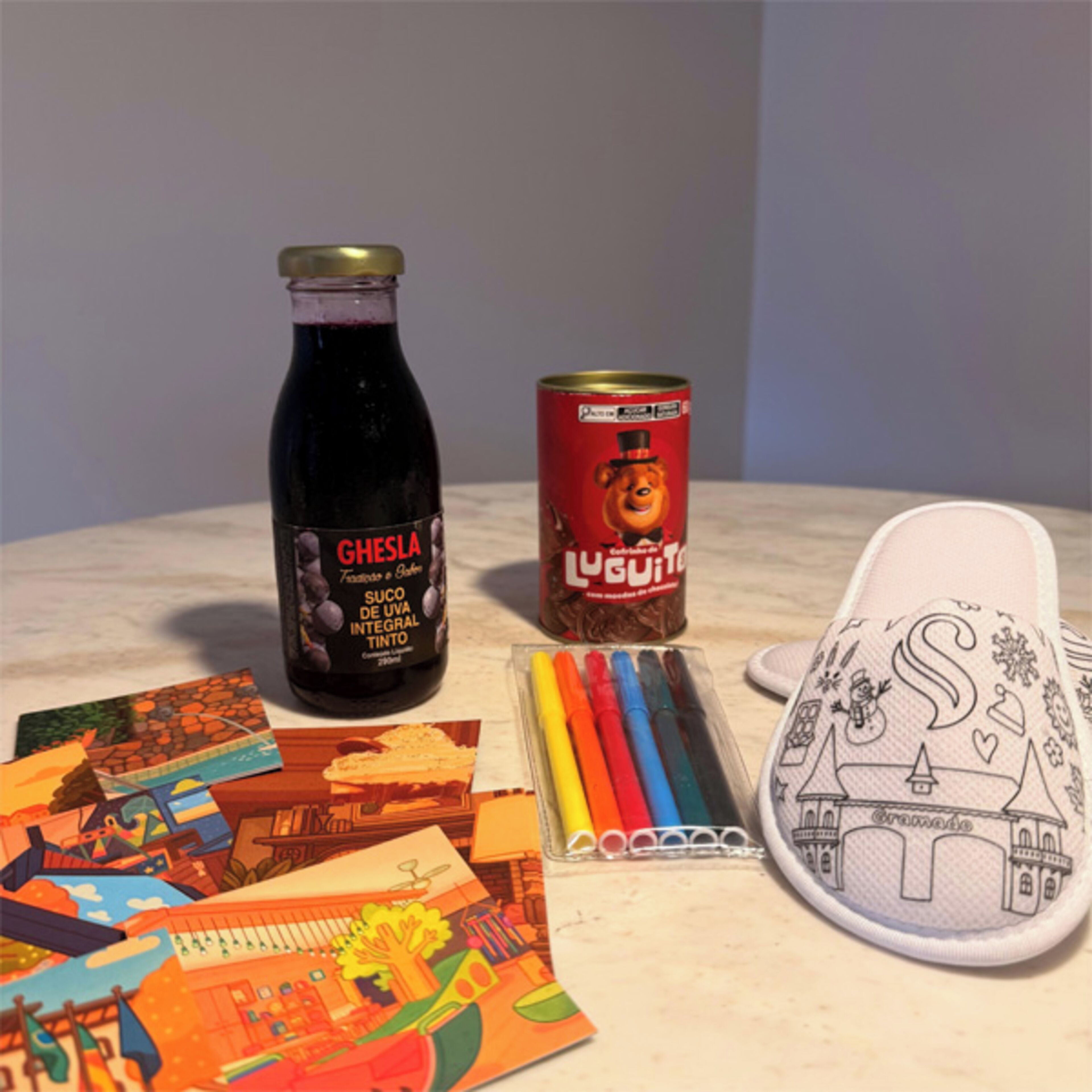 A bottle of Ghesla wine, a can of Lugui, and a drawing pad with colored pencils.