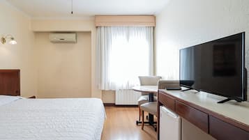 Une chambre d’hôtel avec un lit, un bureau avec une télévision, une chaise et une fenêtre avec des rideaux.