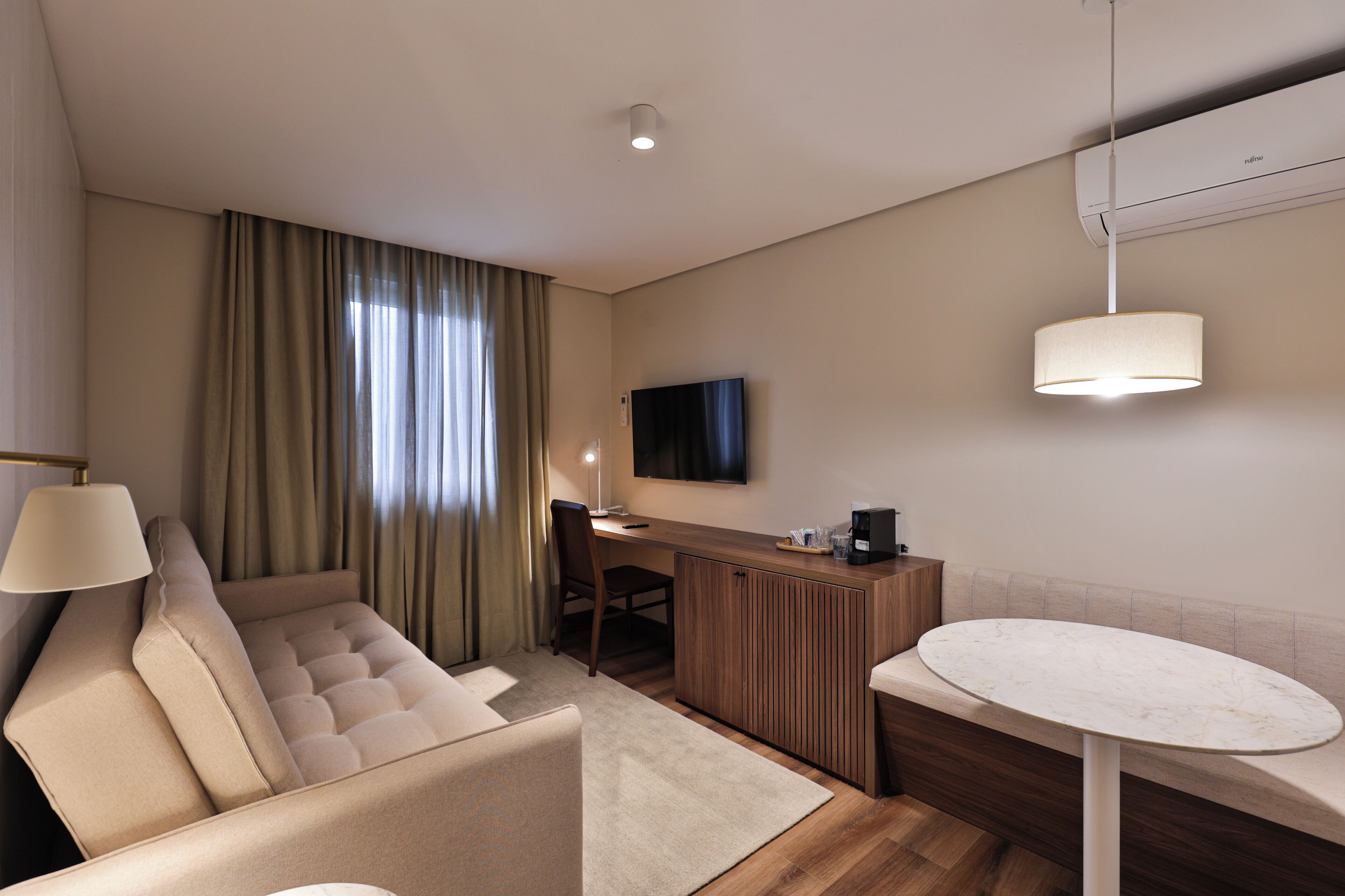 A modern hotel room with a sofa, a desk, a television, and a dining table.