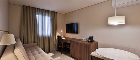 A modern hotel room with a sofa, a desk, a television, and a dining table.