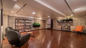 A spacious room with a wooden floor, a black leather sofa, an orange chair, a bookshelf, and a plant.