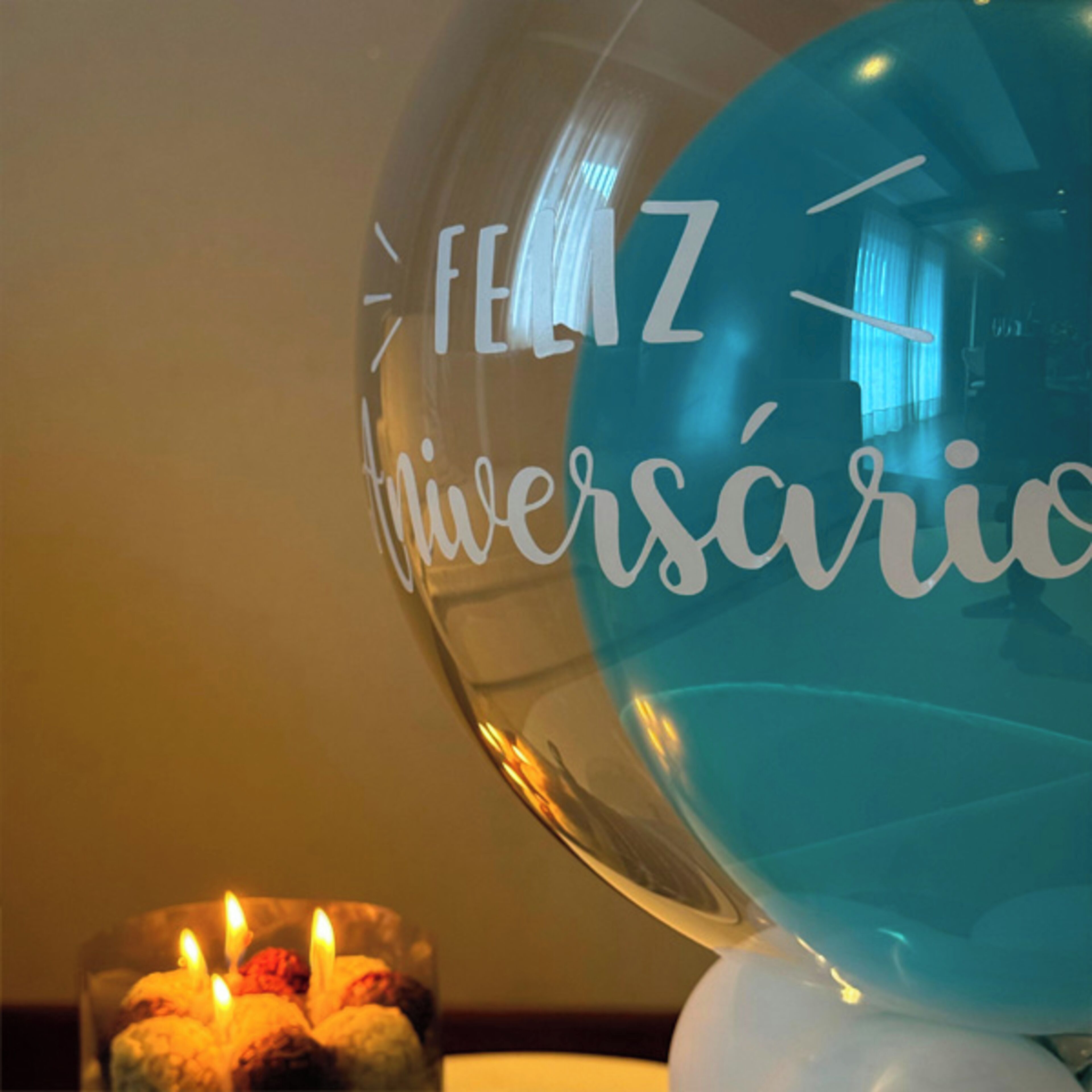 Un globo de vidrio transparente con la inscripción "Feliz Aniversário", colocado sobre una mesa junto a una vela encendida.