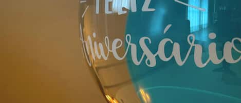 Un globo de vidrio transparente con la inscripción "Feliz Aniversário", colocado sobre una mesa junto a una vela encendida.