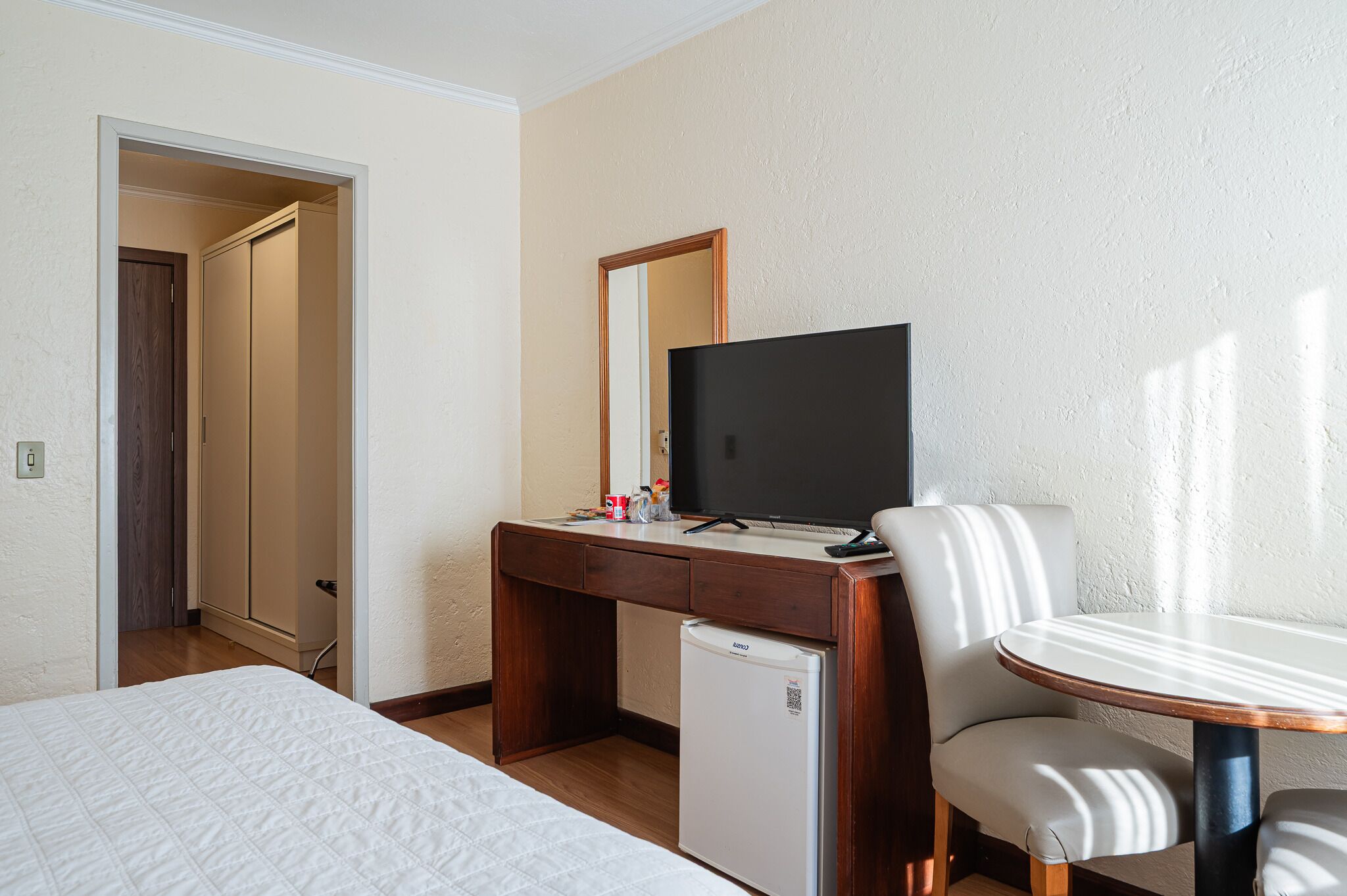 Una habitación de hotel con una cama, un escritorio con televisor, un refrigerador y una silla.