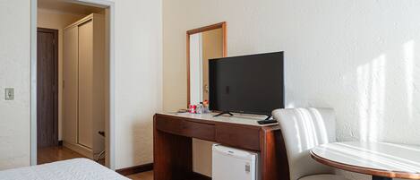 A hotel room with a bed, a desk with a television, a refrigerator, and a chair.