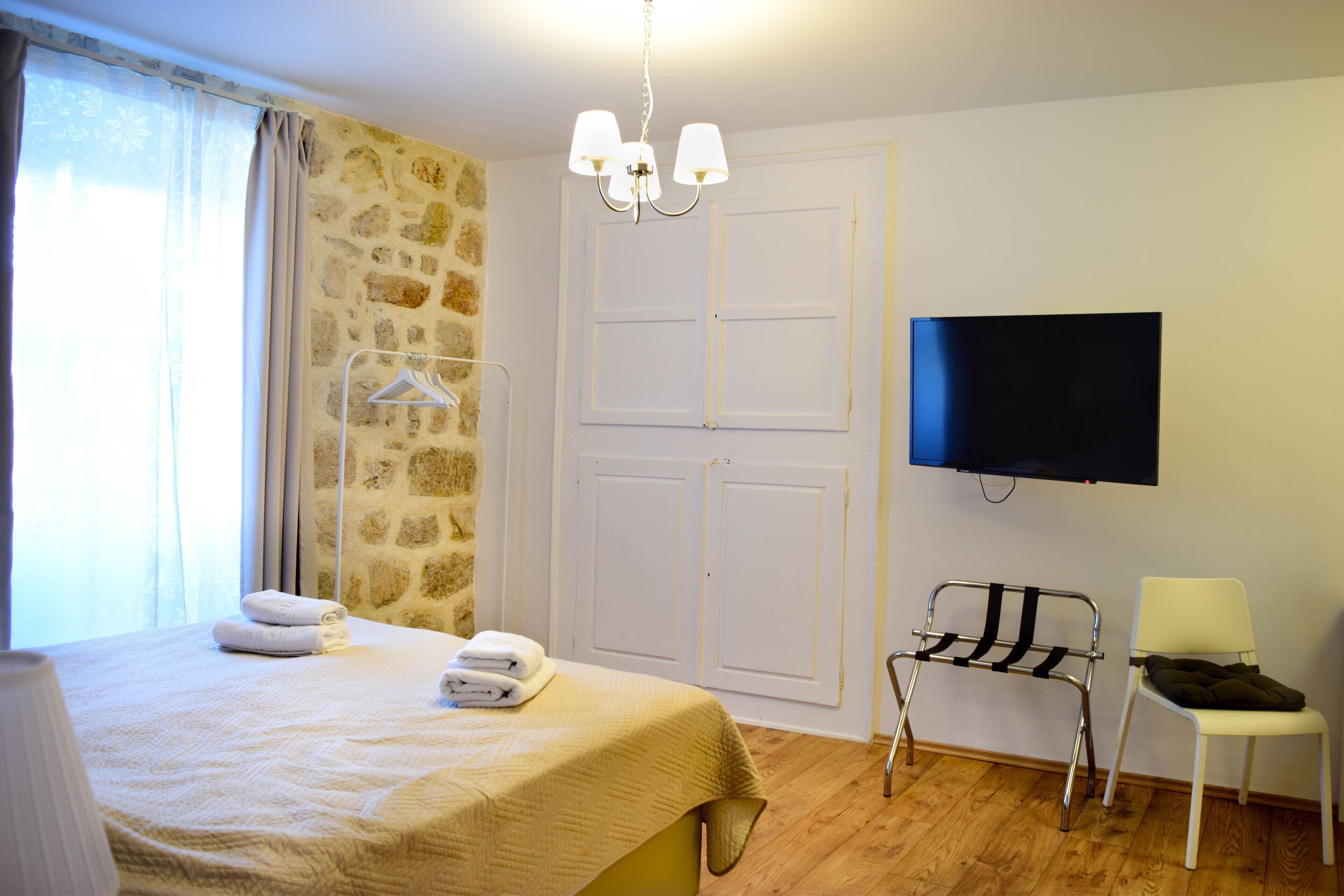 A hotel room with a bed, a TV, a chair, a hanging clothes rack, and a stone wall.