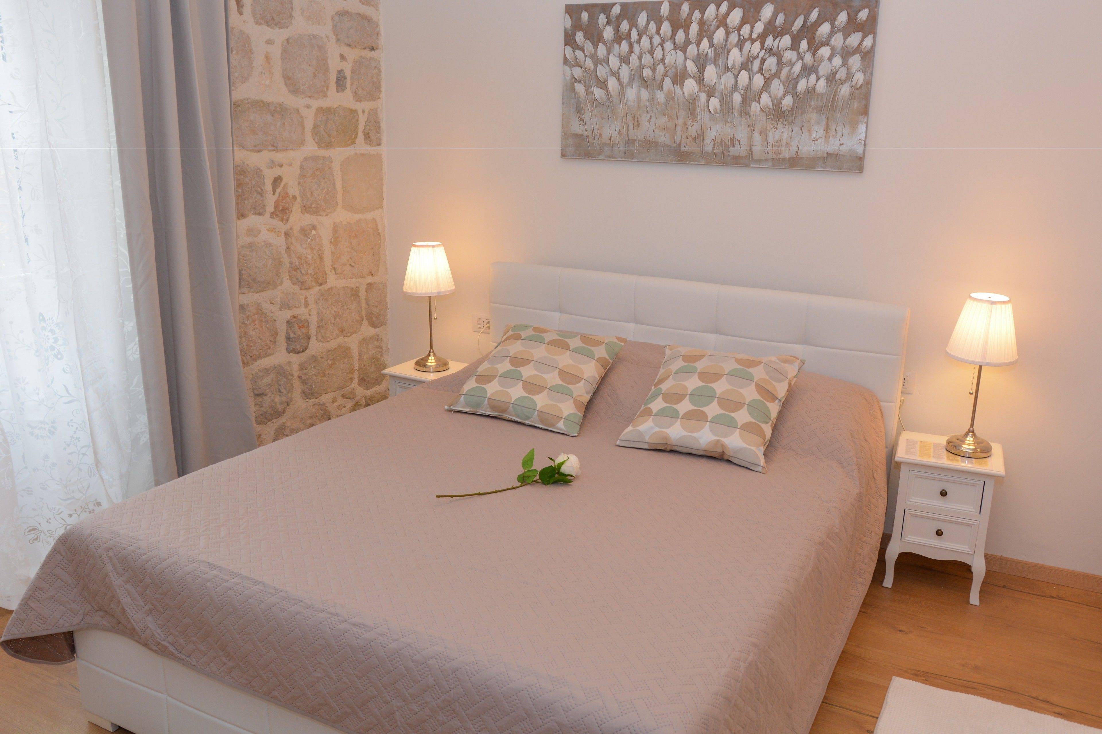 A neatly made bed with two pillows, a bedside table with a lamp, and a wall with a floral painting.