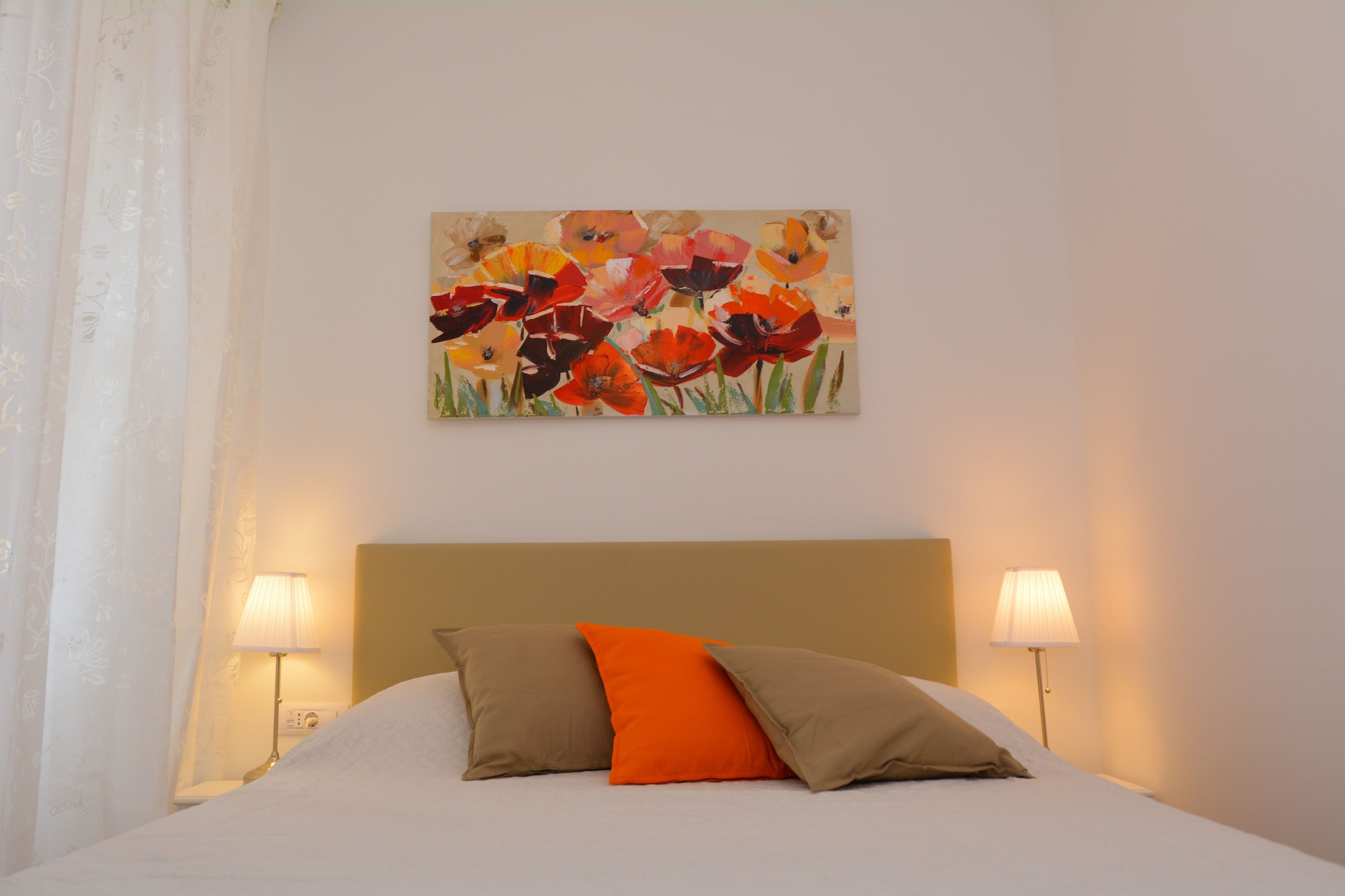 Una habitación de hotel con una cama, dos lámparas de noche y un cuadro floral en la pared.