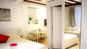 A hotel room with a bed, a desk, and a second bed. There is a door leading to another room. - Rilati Old Town Palace (Dubrovnik)