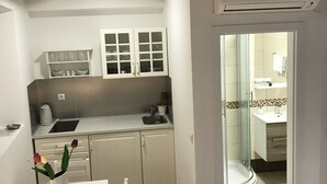 A compact kitchen with white cabinets, a sink, and a dining area with a table and chairs. - Rilati Old Town Palace (Dubrovnik)