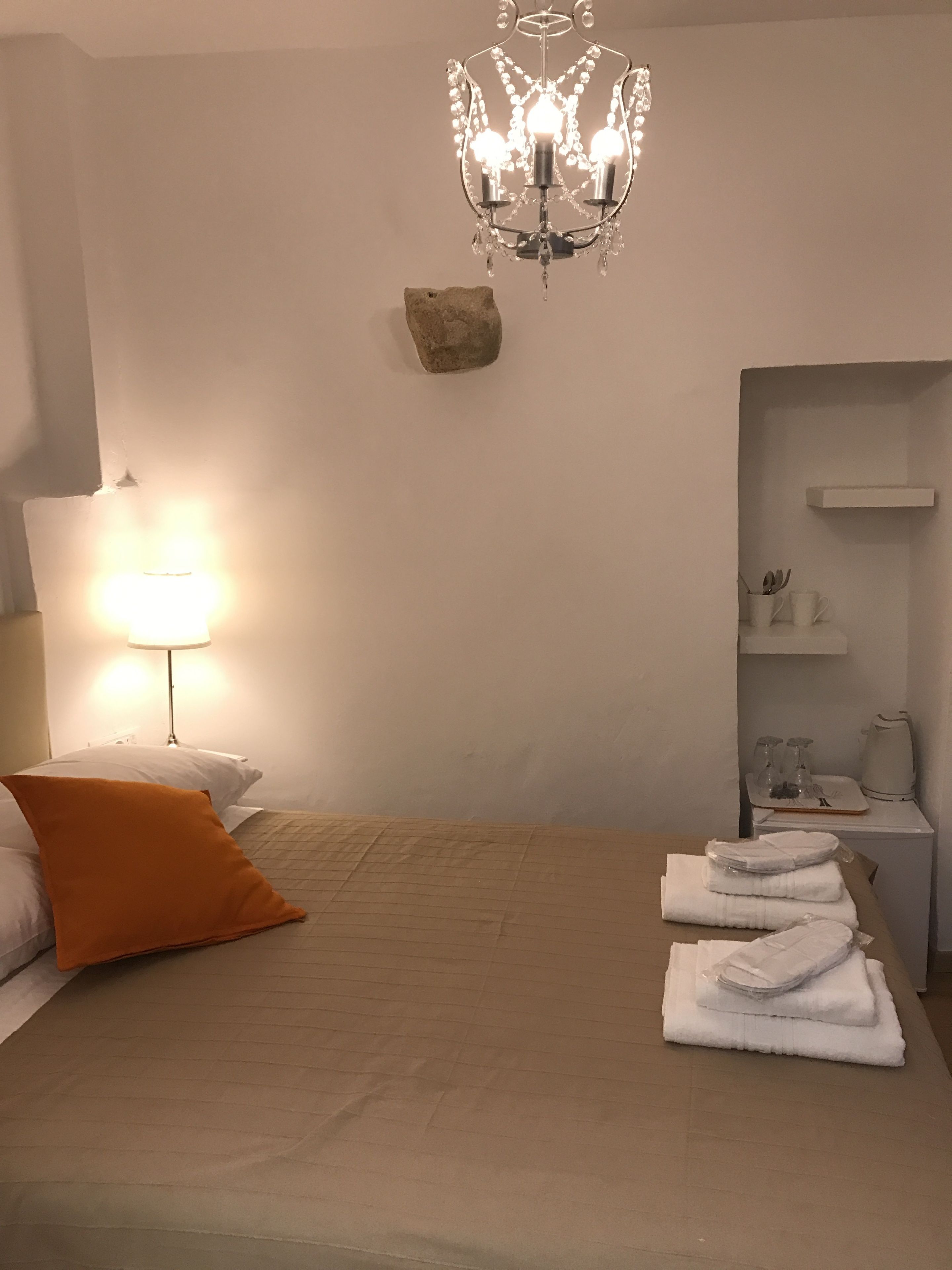 A bedroom with a bed, a nightstand, a lamp, a chandelier, a rock decoration, and a bathroom area with a towel rack.