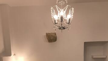 A bedroom with a bed, a nightstand, a lamp, a chandelier, a rock decoration, and a bathroom area with a towel rack.