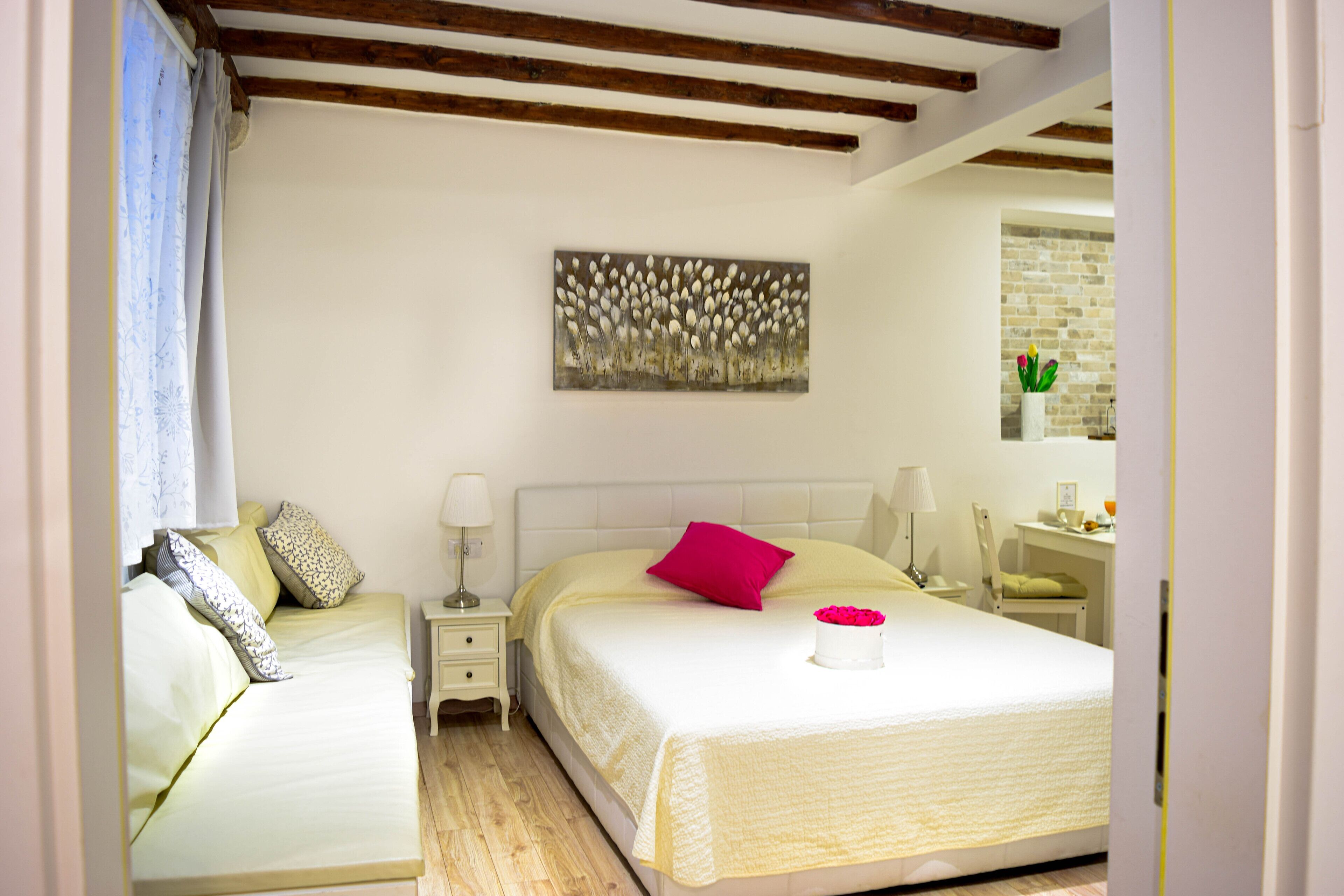 A bedroom with two beds, a nightstand, a lamp, a painting on the wall, and a brick wall in the background.